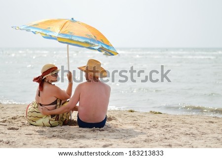 Happy mature couple sitting at seashore on sandy beach back to back