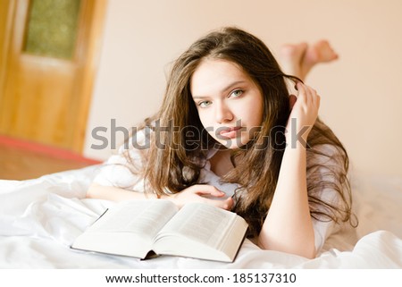 attractive brunette young woman beautiful girl in bed with book looking at camera