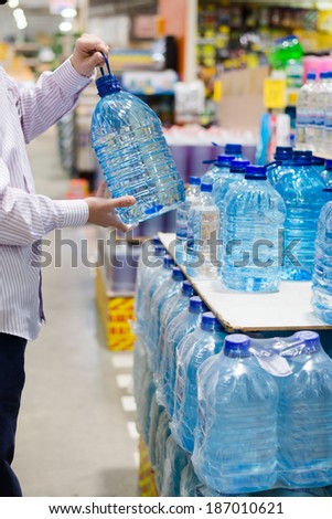 man in shirt choosing, selecting or buying a bottle of mineral drinking or distilling water at the shopping store focus on hands on the supermarket display shelf background