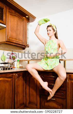 sitting on the table in the kitchen wearing apron beautiful pinup sexy brunette young woman dancer or performer having fun posing hand up image