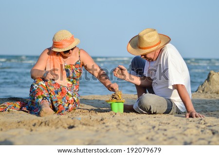 picture of happy mature couple, man & woman, having fun playing at seashore with children toys on sandy beach summer sea outdoors background