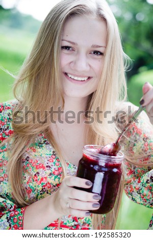 picture of eating strawberry jam from glass jar beautiful blond young woman having fun happy smiling & looking at camera teenage girl on summer day outdoors background