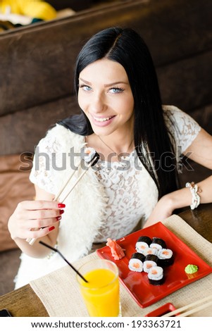 smiling sushi: closeup image of gorgeous brunette young woman eating tasty Japanese sushi having fun sitting & happy looking at camera on restaurant interior background