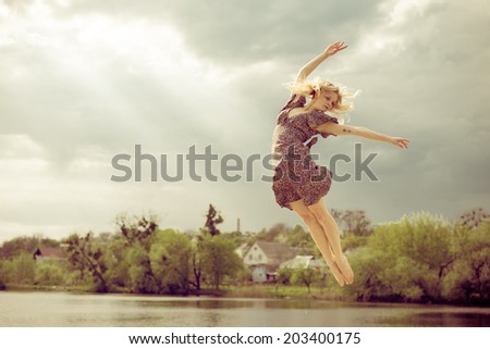 joyful freedom: portrait of beautiful blond dancing young woman with falling sun light rays from blue sky at river or water lake on spring or summer nature green outdoors background copy space picture