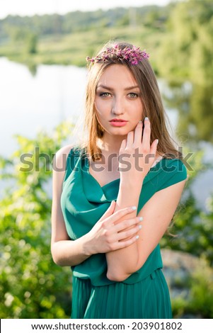 portrait of pretty fairy: young lady cute girl having fun posing in green dress with pink wreath of flowers & sun light rays sensually looking at camera on summer outdoor copy space background