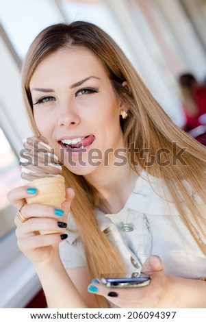 holding mobile phone & eating delicious ice-cream one beautiful young business woman having fun relaxing in restaurant or coffee shop happy smiling licking lips & looking at camera close up portrait