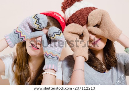portrait of playful happy smiling young women girl friends having fun wearing knitted gloves and hat showing glasses sign on light copy space background