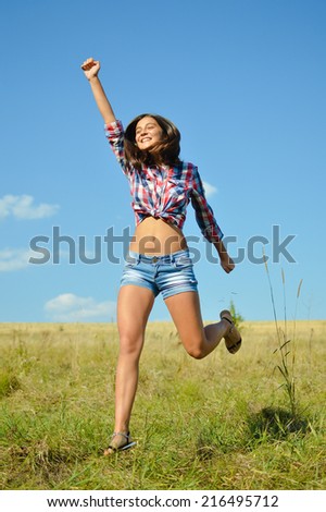 jumping joy: sexy pretty girl in jeans shorts running high and happy smiling on blue sky outdoors copy space background, portrait