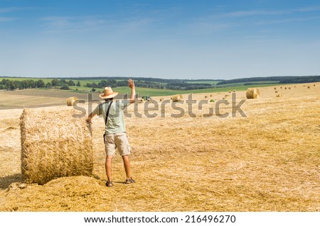 picture of man standing in the golden field of rounded hay stock on summer blue sky copy space background