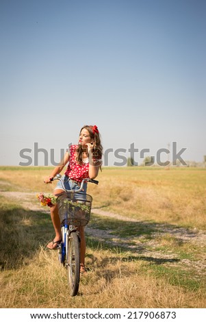 Beautiful pinup girl in the fields having fun with bicycle & flowers in basket under bright blue summer sky on summer outdoors copy space background