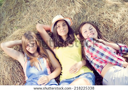 3 pretty girls having fun relaxing lying on hay happy smiling with excellent white teeth & looking at camera on green summer outdoors copy space background