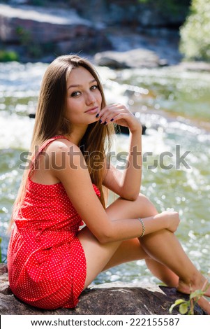Young woman sitting on rock in fast mountain river and having fun on summer or early autumn outdoor copy space background