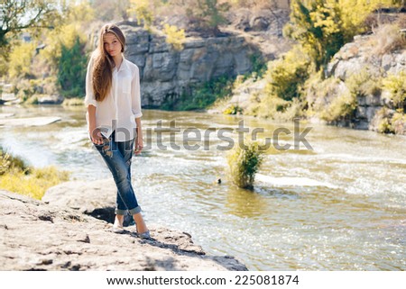 Young woman standing on cliff edge over fast mountain river on summer or early autumn outdoor copy space background