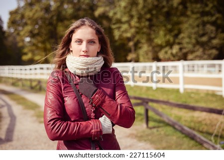 autumn beauty: sexy young pretty lady in leather jacket on cold windy day on white barn fence copy space background