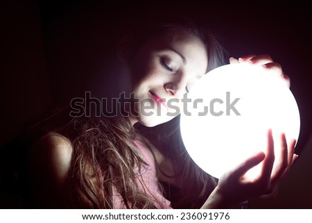 closeup image of beautiful young sleeping woman holding ball of light and happy smiling