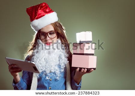 young pretty lady in Christmas hat, glasses and beard holding gifts and looking at tablet pc computer
