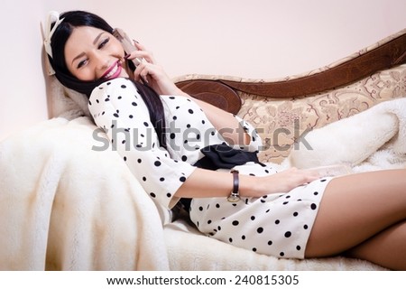 attractive pretty sexy young lady talking on the mobile cell phone looking at camera & happy smiling relaxing on sofa