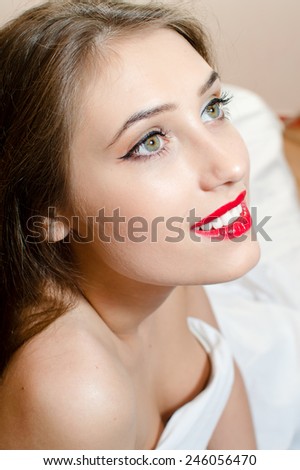 close up of beautiful woman with green eyes and red lips looking up smiling in bed