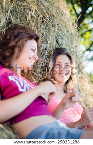 Picture of 2 beautiful young women girls friends having fun lying on haystack happy smile on green outdoors background