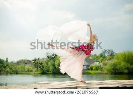 Picture of beautiful young lady in light dress dancing at water side on sun rays blue sky outdoors background