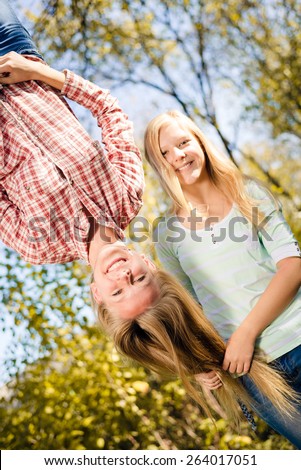 Girls having fun in park hanging upside down on green copy space background