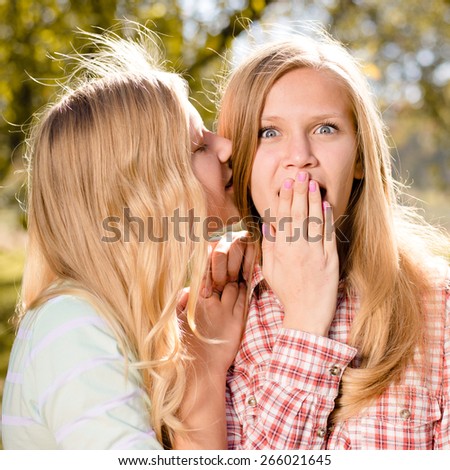 Two happy young women teen girl friends whispering secret on bright sunny day outdoors
