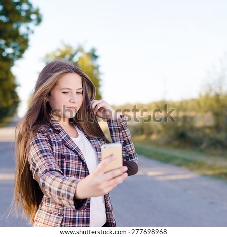 Happy girl taking selfie picture with smartphone outdoors or looking in mirror