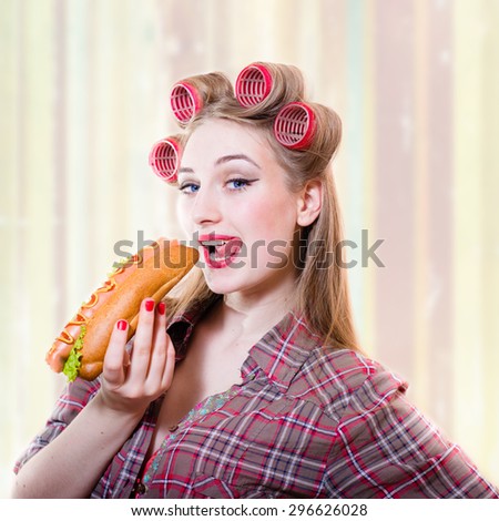 Portrait of beautiful girl in hair curlers with her mouth open and hot dog in her hand