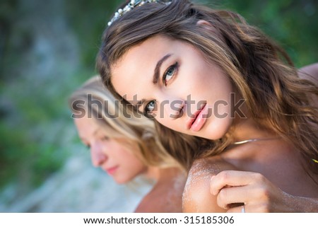 Potrait of two sensual young ladies standing back-to-back