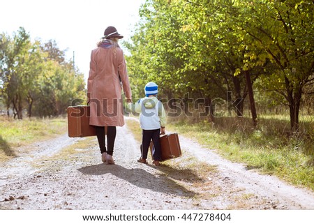 Back view of female wearing hat with child walking away on rural road. They carrying old suitcase over sunny outdoors background Imagine de stoc © 