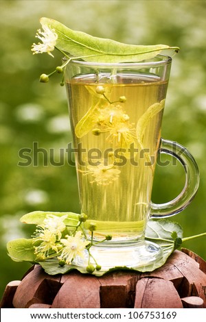 A cup of linden tea with linden flowers outdoors
