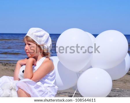 The cute little blonde girl in a white dresses with white balloons on the beach