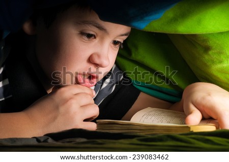 boy reading a book under the covers
