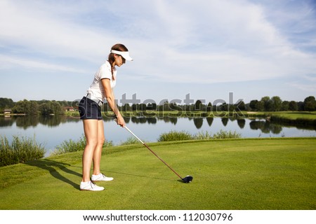 Girl golf player focusing on golf ball to tee off in tee-box.