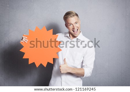 Excellent offer: Joyful salesman giving thumbs up at empty sign with space for text promoting sales isolated on grey background.