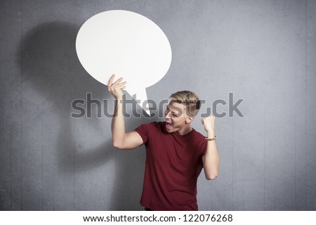 Excellent news: Overjoyed successful man holding white blank speech bubble with space for text isolated on grey background.