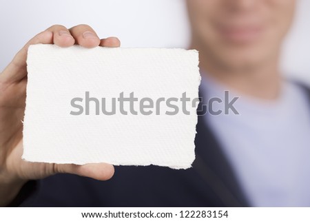 Closeup of white blank card with space for text in hand of a smiling blurred man in background.
