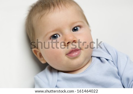 Close up portrait of sweet baby boy with blue eyes and blue shirt looking straight.