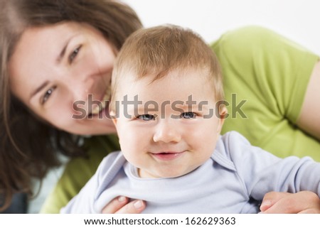 Happy family: Adorable joyful baby boy laughing while sitting in his mother arms, mother blurred in background.