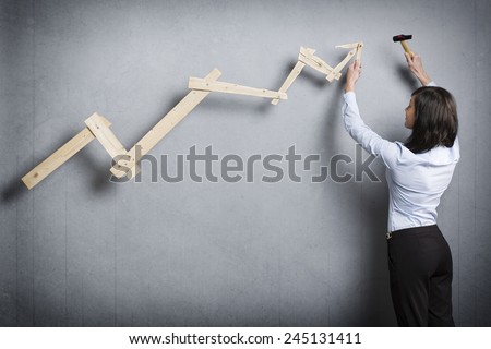 Concept: Building your own successful career or business. Confident businesswoman with hammer in hand building  business graph with positive trend, isolated on grey background.