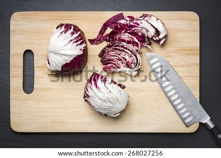 Purple cabbage cut on a chopping board with knife, isolated on stone plate.