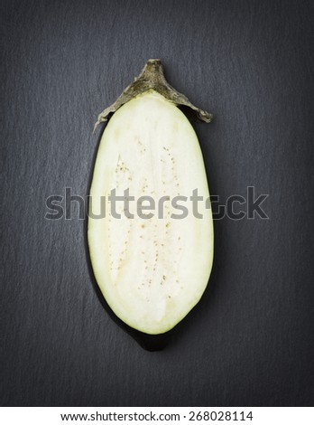 Sliced eggplant showing its white fruit flesh, isolated on stone background.