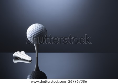 Stylish golf ball on tee with tees lying aside, isolated on dark blue background with reflection, empty copy space for text.