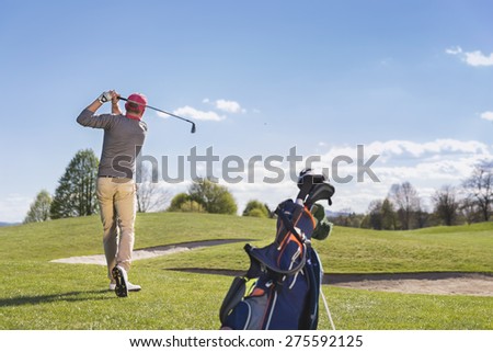 Male golf player swinging golf club, with golf bag and beautiful fairway in background.