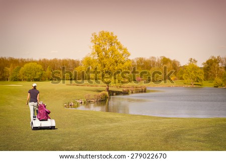 Woman golf player walking on fairway with lake at sunset.