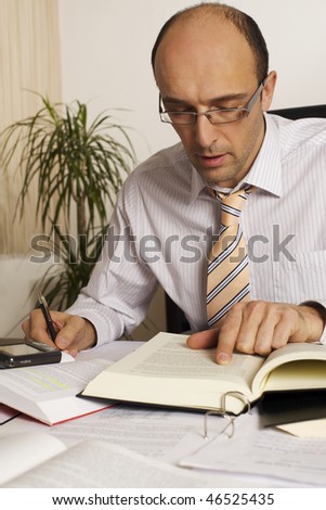 Male professional sitting at desk in office being busy studying books and papers.