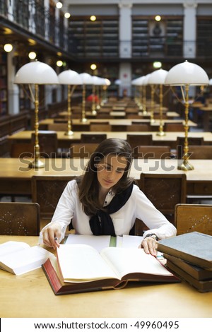 Young attractive woman sitting at desk in old university library studying books, front view.