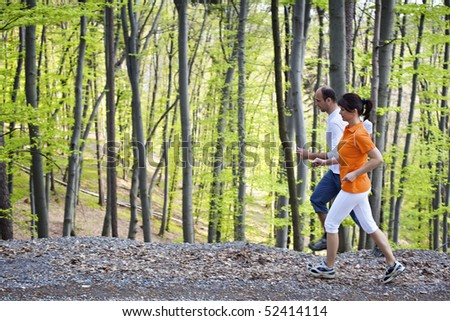 Woman and man jogging on gravel path beside each other with green beech forest in background.