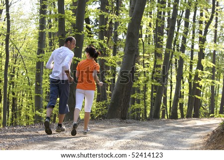 Happy couple jogging together on gravel path in beech forest, view from behind.
