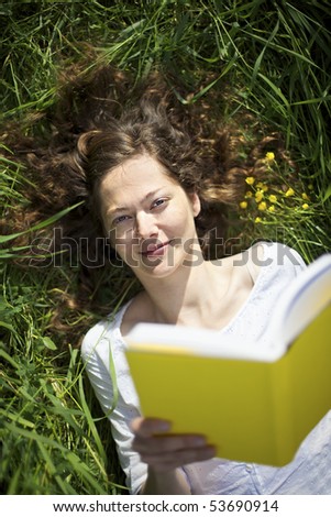 Young smiling woman lying in meadow and reading a book, top view.